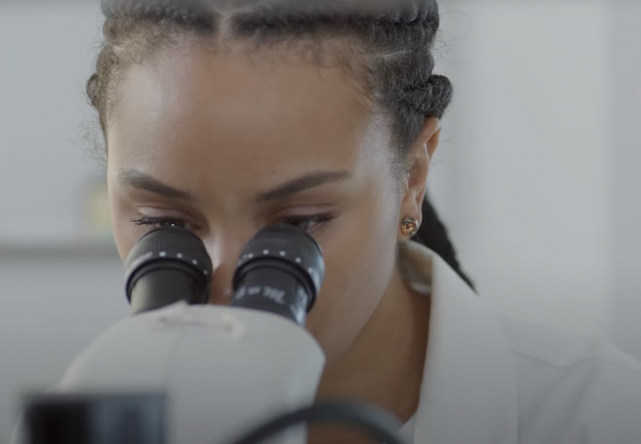 a biracial black woman with cornrow braids peers into a microscope in the lab.